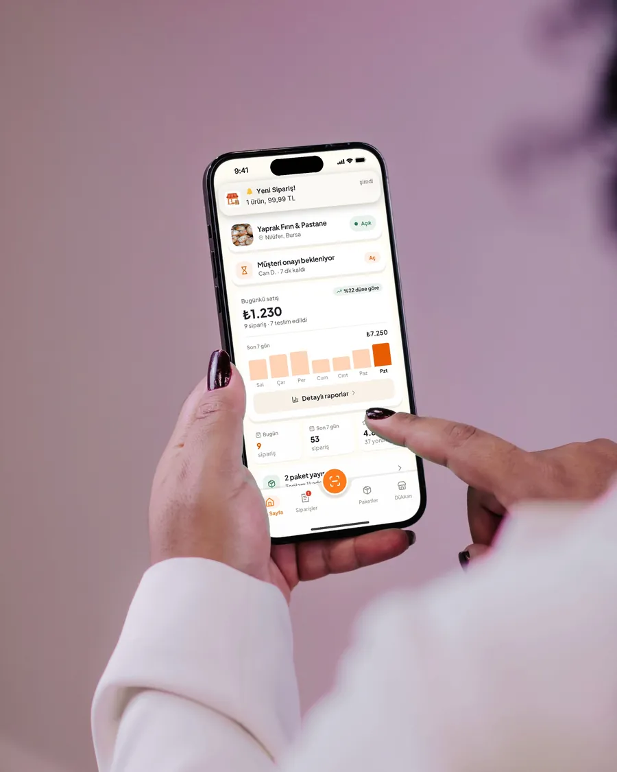 İşletme sahibinin elindeki iPhone’da Ye Gitsin İşletme ana sayfası ve “Yeni Sipariş!” bildirimi